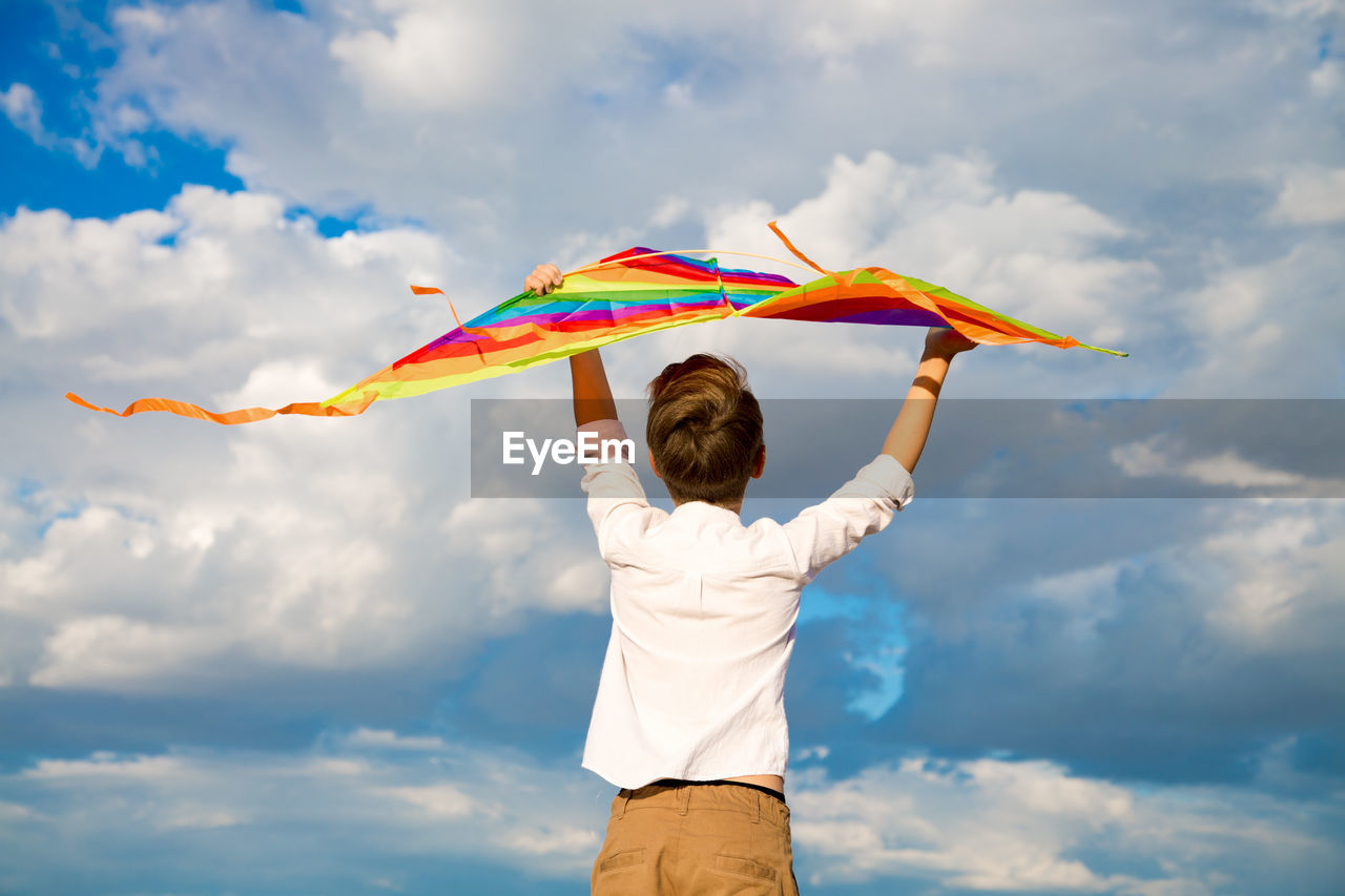 A handsome boy a white shirt with a multicolored kite on a blue sky background.