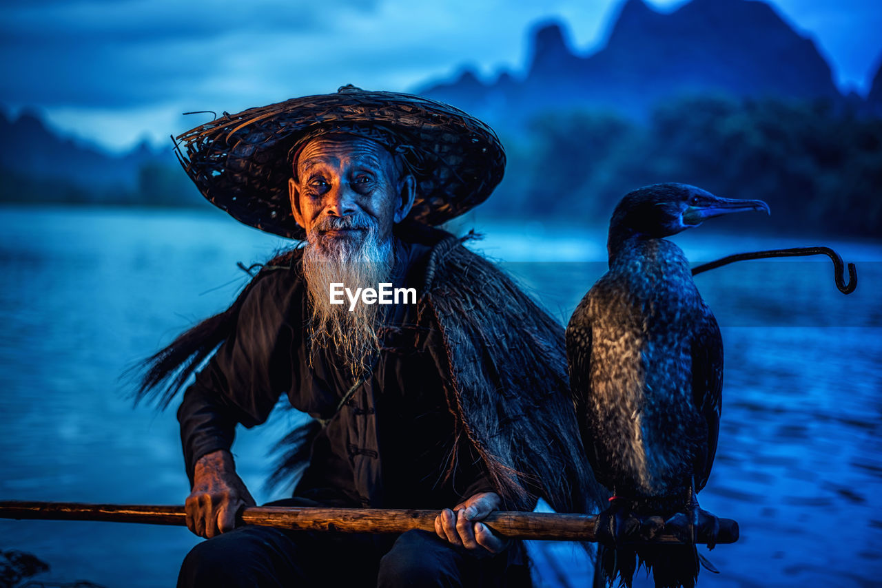 Bird perching on stick held by man in lake
