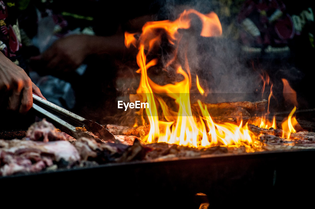 Cropped hand of man holding serving tongs by burning barbecue