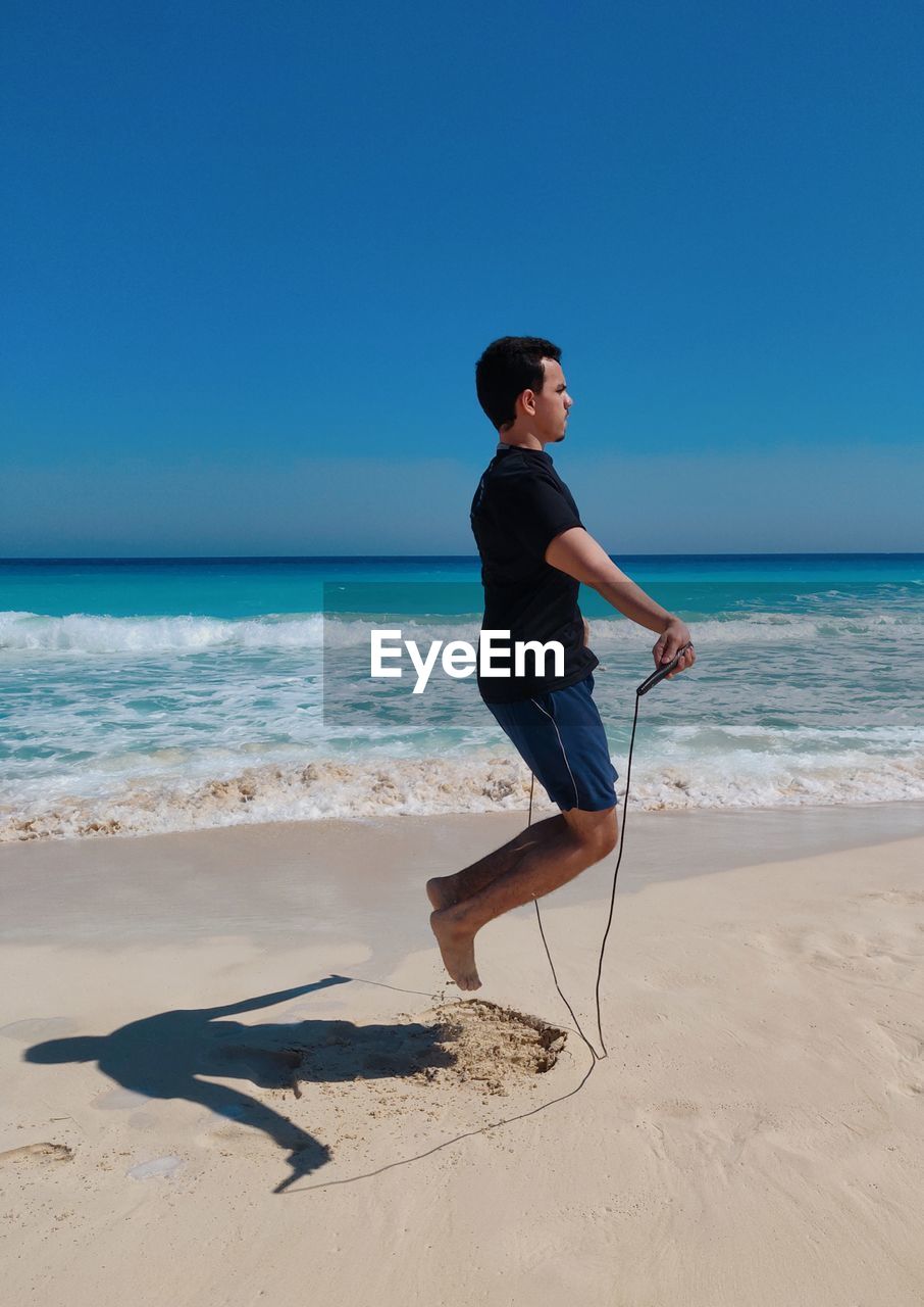 Man  skipping rope on beach against sky