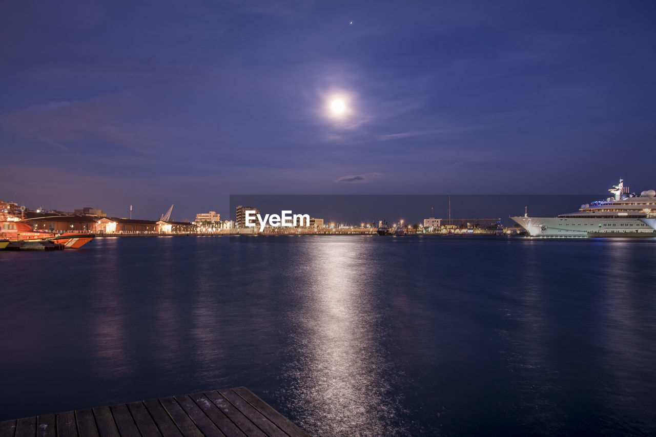 Pier over river against illuminated cityscape during night