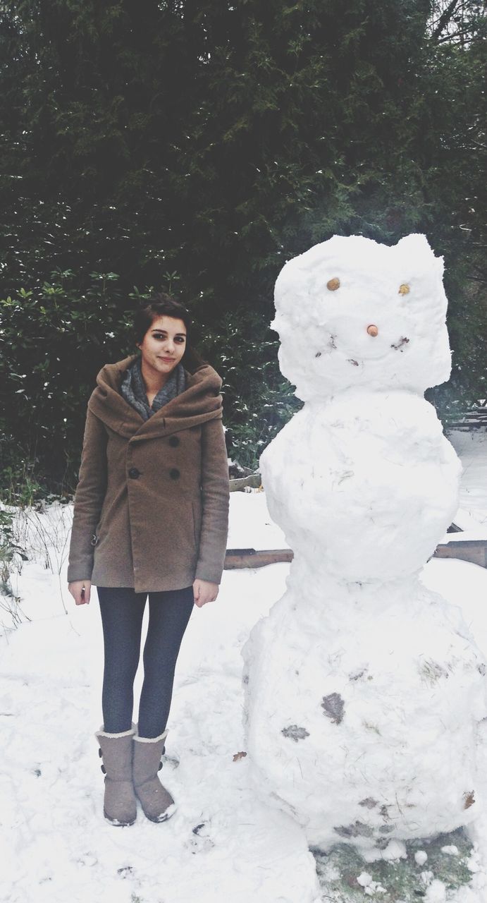 Full length portrait of woman standing by snowman on field