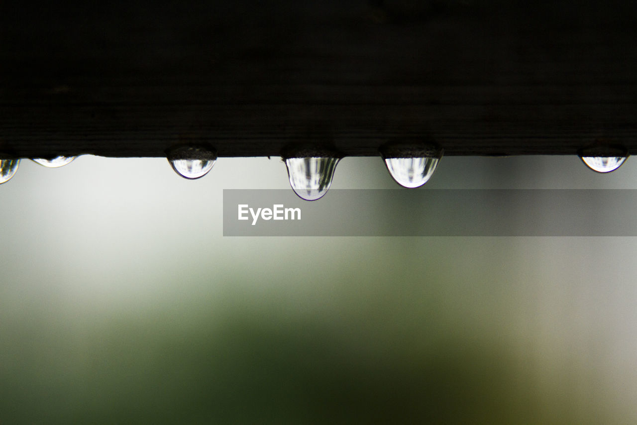 Rain drops hang from the roof with blur nature background.