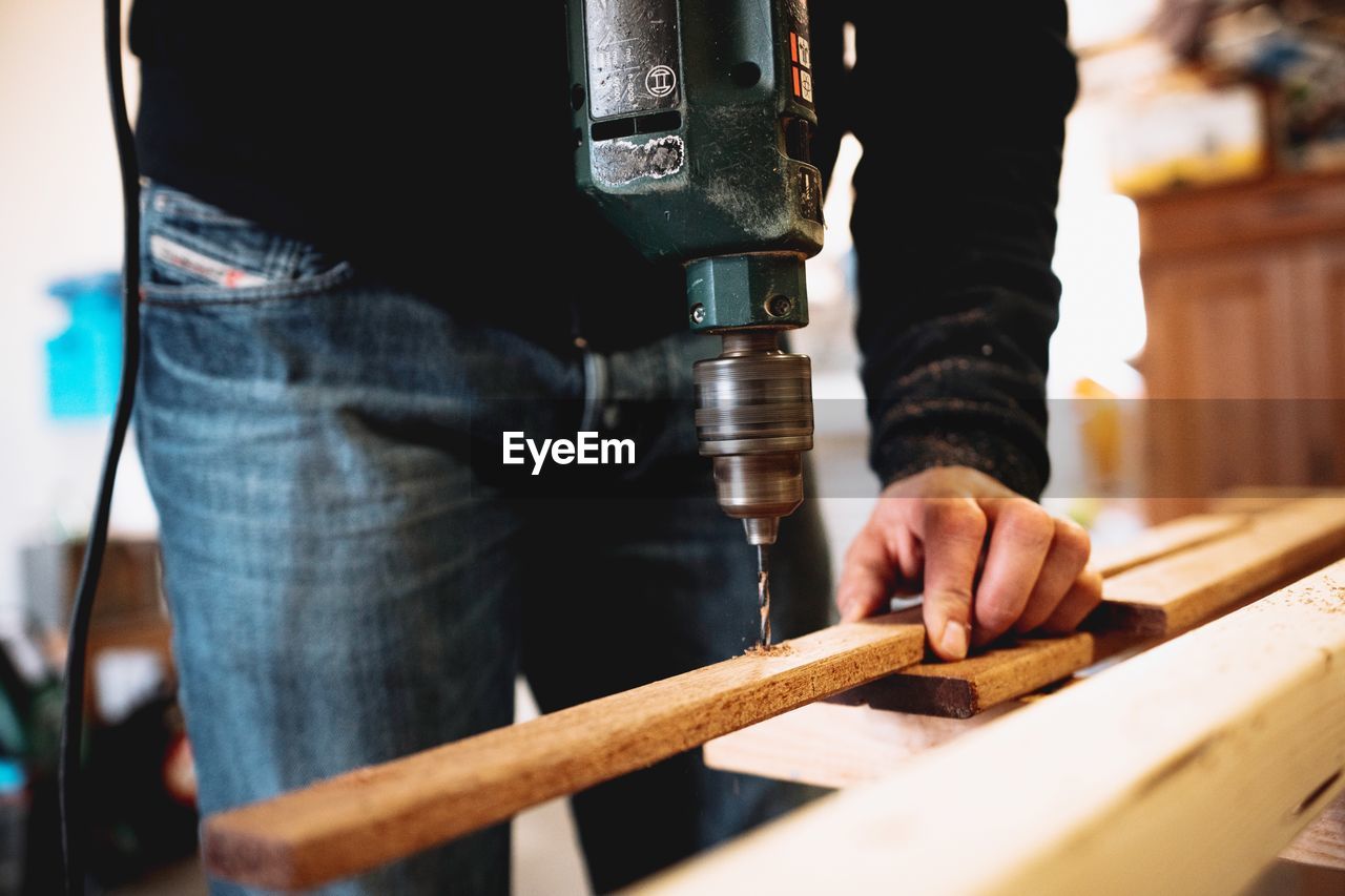 Midsection of man drilling wood at workshop