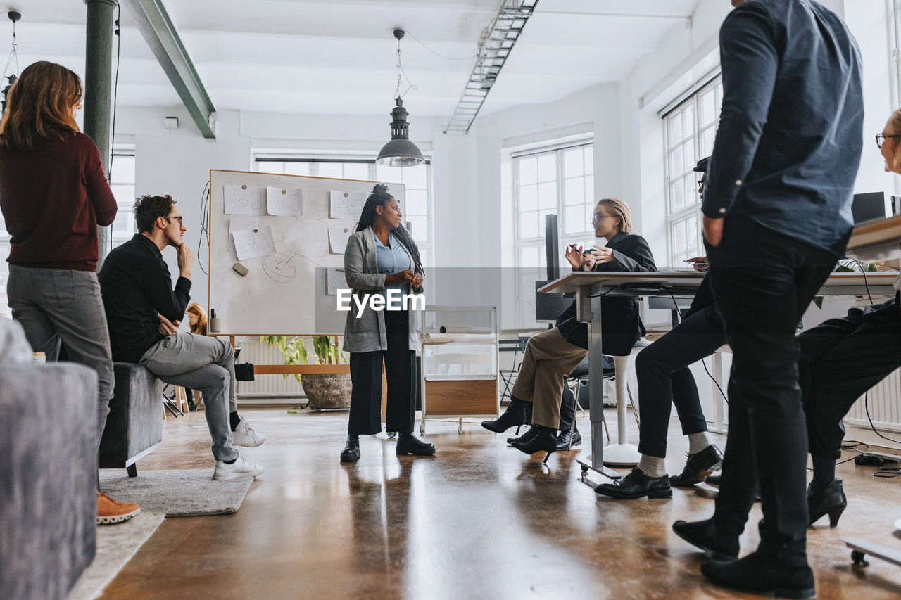 Multiracial colleagues listening to businesswoman explaining strategy during meeting in office