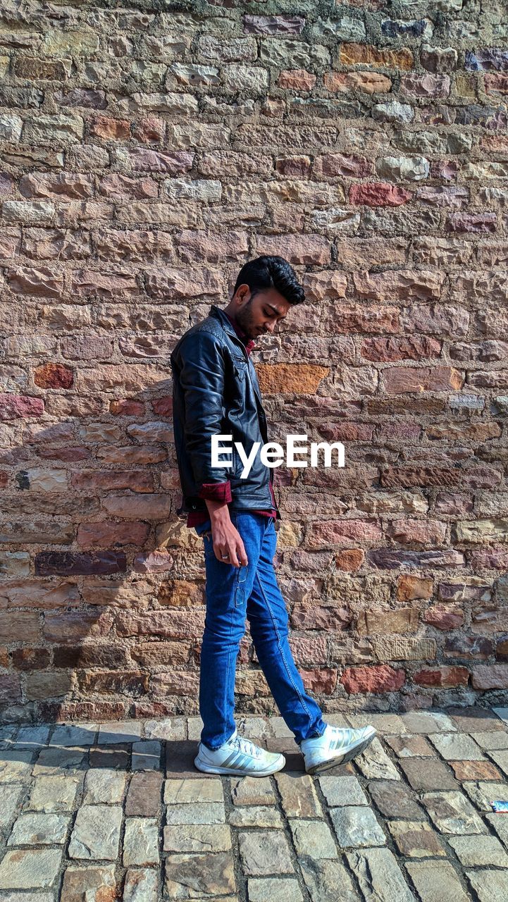 FULL LENGTH OF YOUNG MAN STANDING AGAINST BRICK WALL