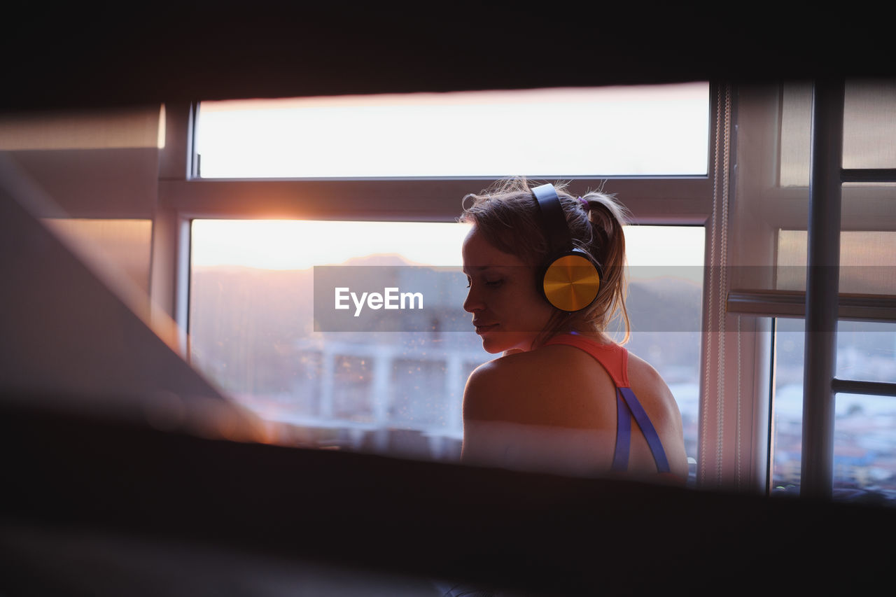 Rear view of woman listening music while sitting by window