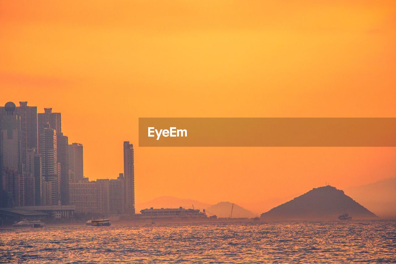 Scenic view of sea by buildings against orange sky