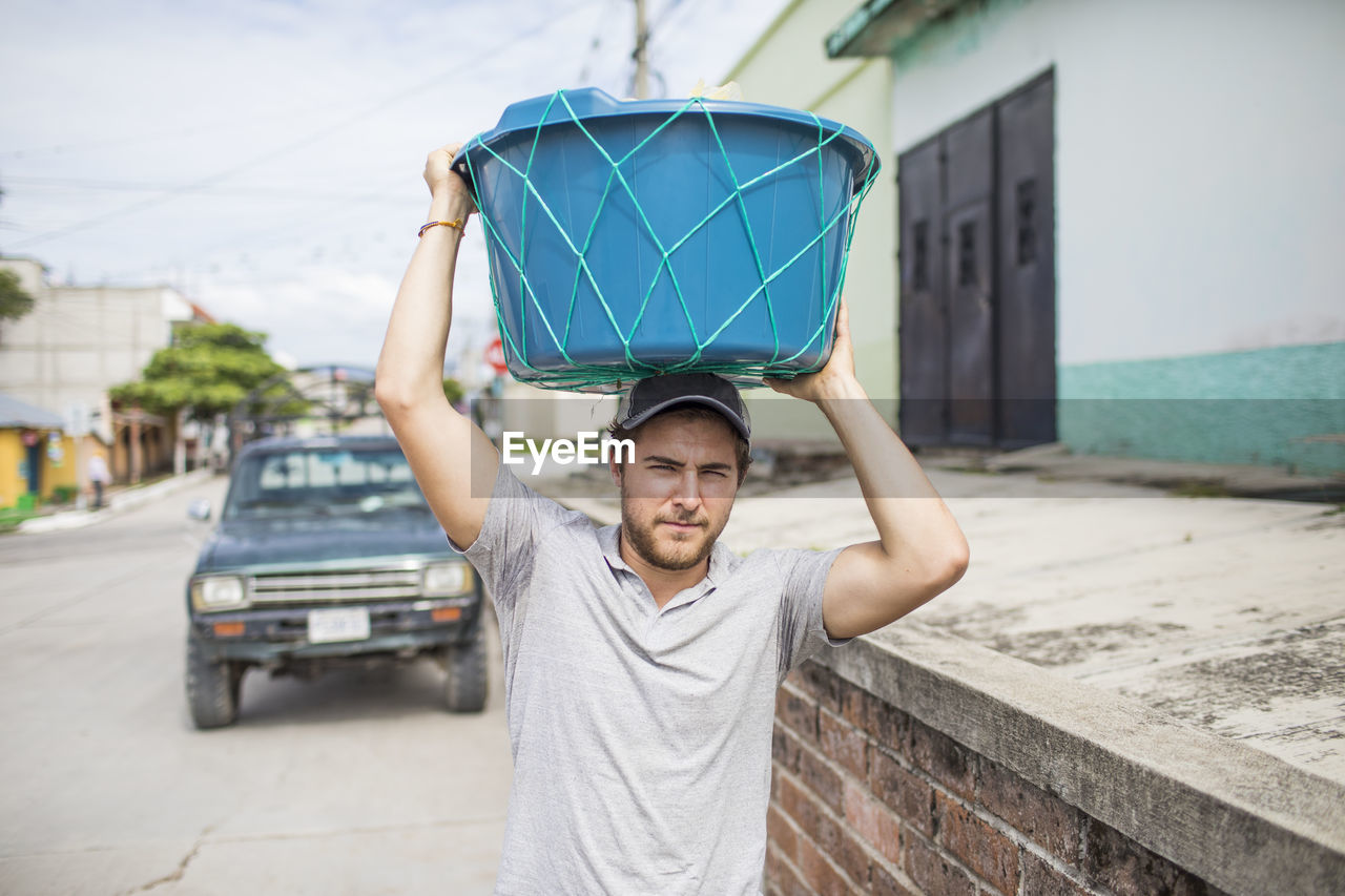 Caucasian man carries basket on top of his head.
