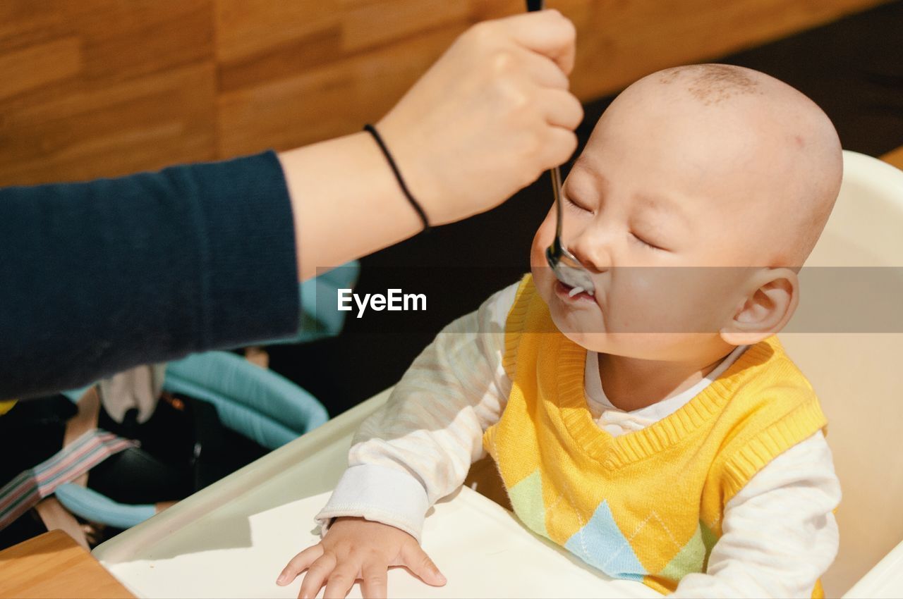 Cropped hand of woman feeding baby sitting on high chair