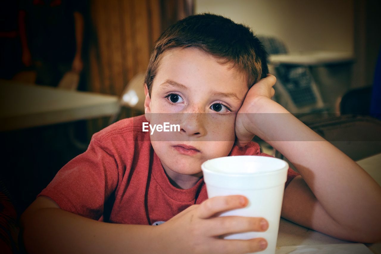 Close-up of thoughtful boy holding glass at home