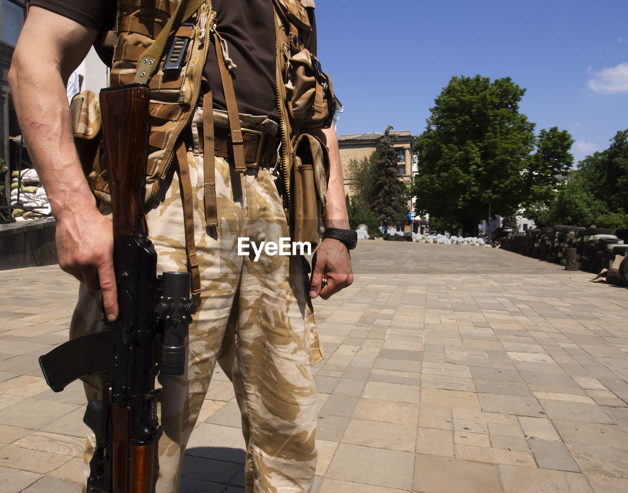 Midsection of military man holding rifle while standing in city