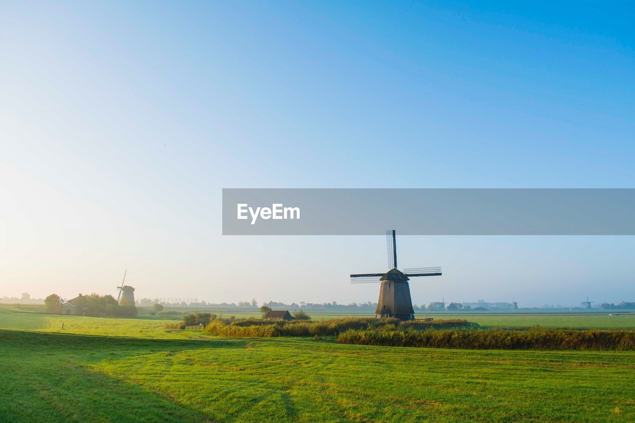 Windmill on field against clear blue sky