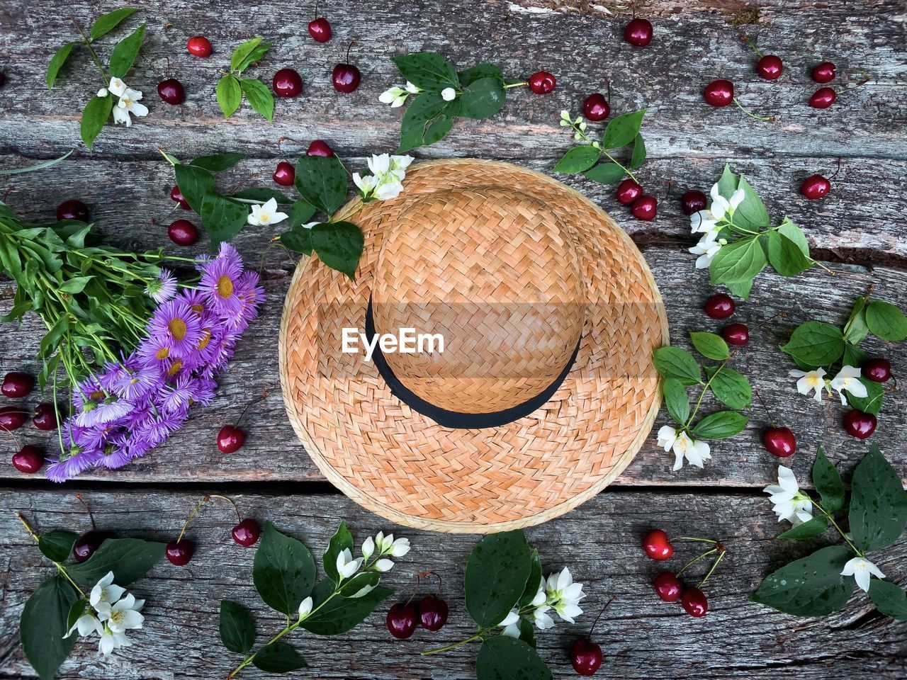 Summer flat lay consisting of straw hat, cherries,purple flowers and jasmine flowers on wooden table