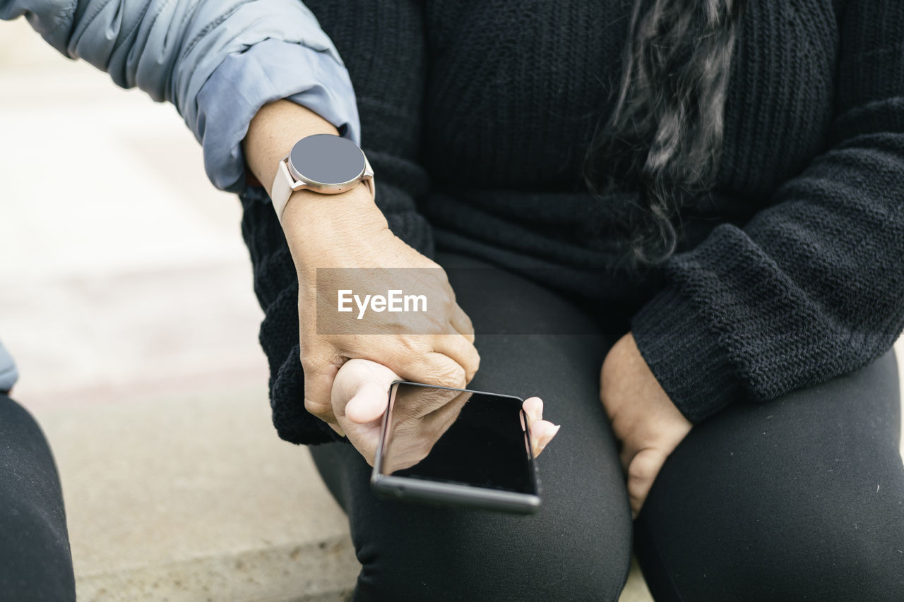 Two spanish-latin women with smartphones and smartwatches, selective focus on the clipped hands.