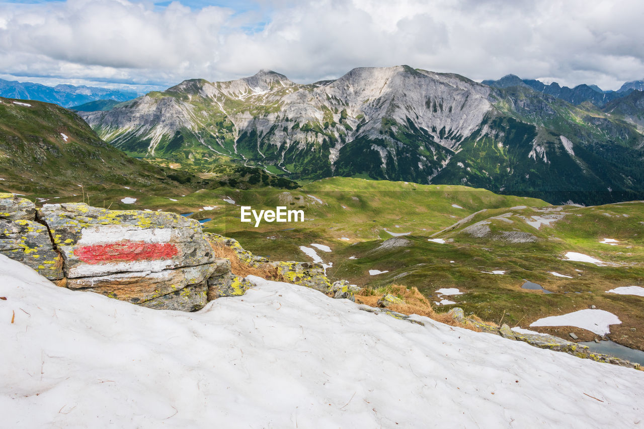 Red and white marking of the hiking trail in the austrian alps. sunny mountain panorama with snow