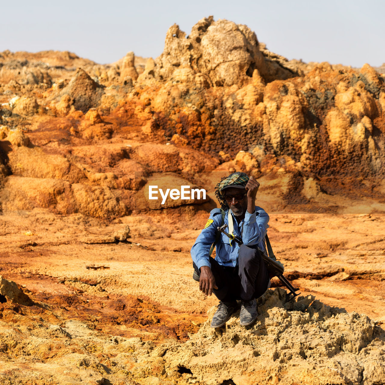 MAN SITTING ON ROCK AGAINST MOUNTAINS