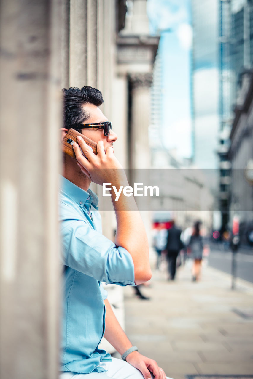 Man answering smart phone while standing in city