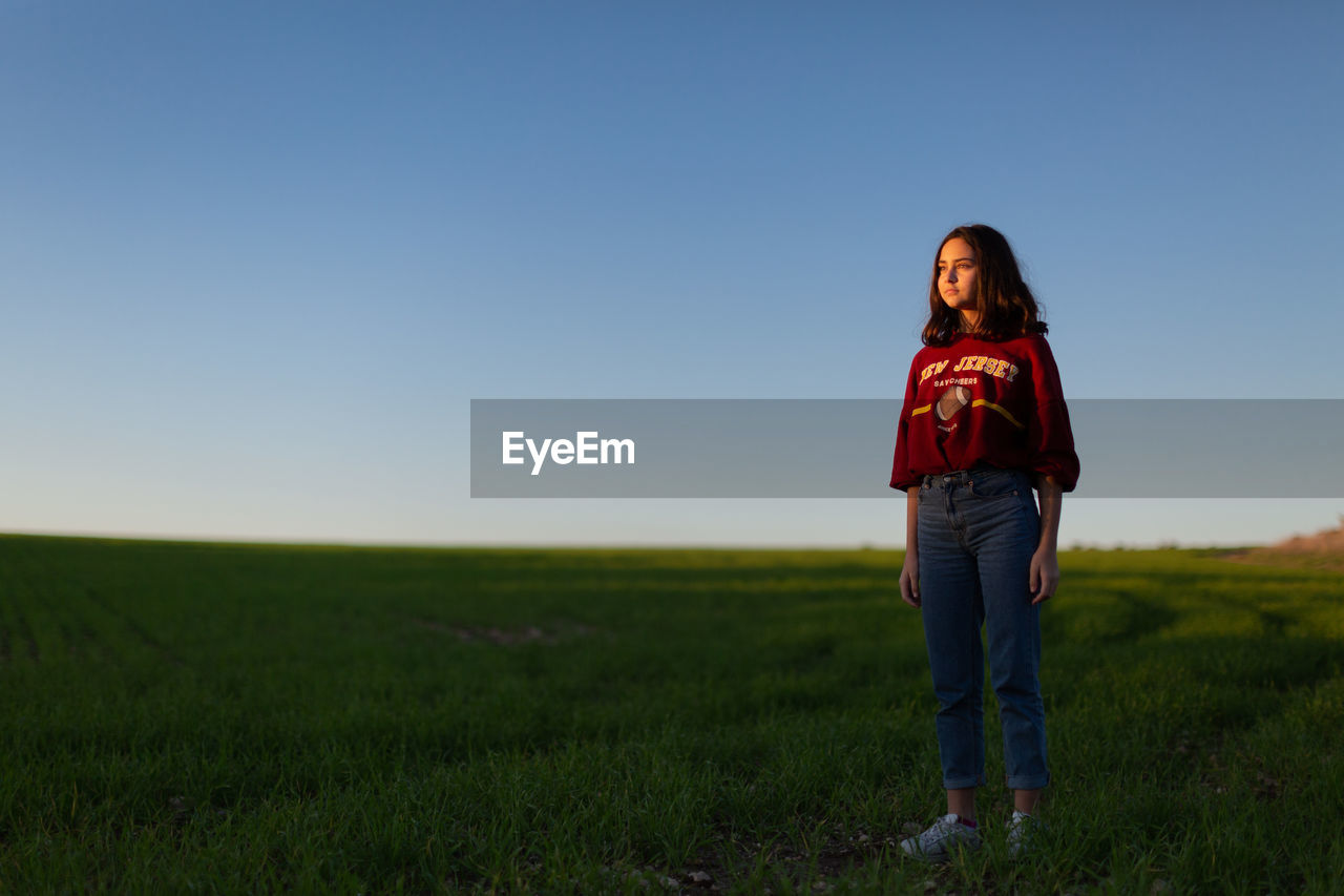 Cute girl standing on grassy field against clear sky