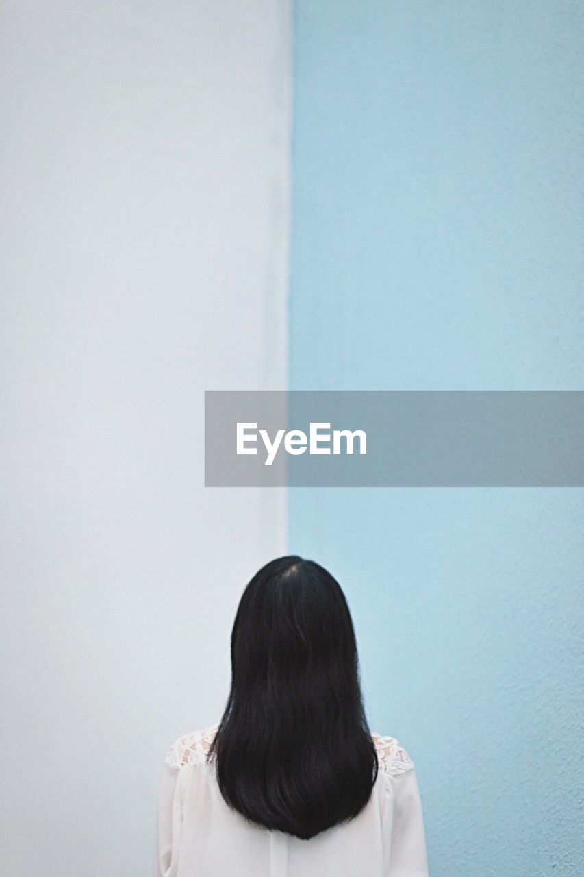 Rear view of woman standing against blue and white wall