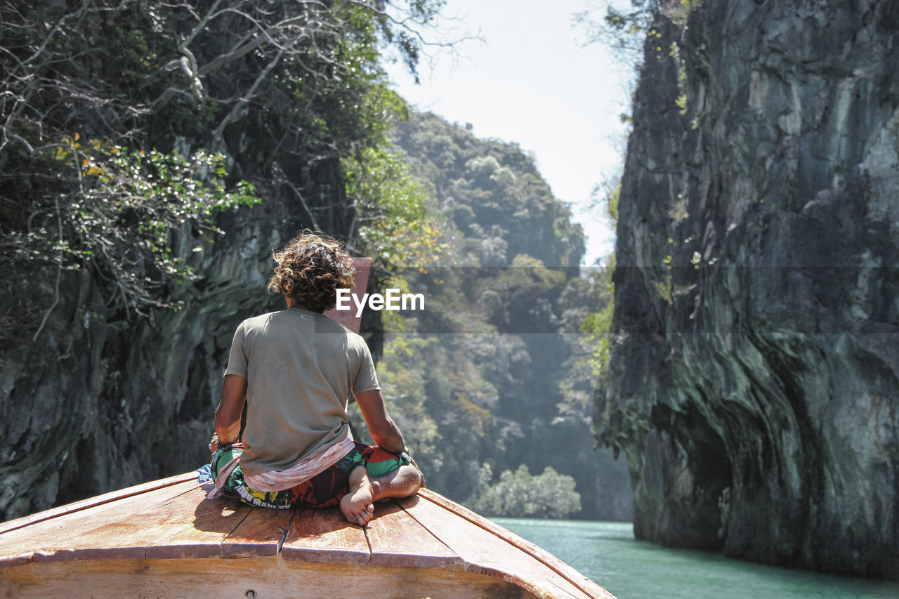 Rear view of man sitting on boat in sea amidst rock formations