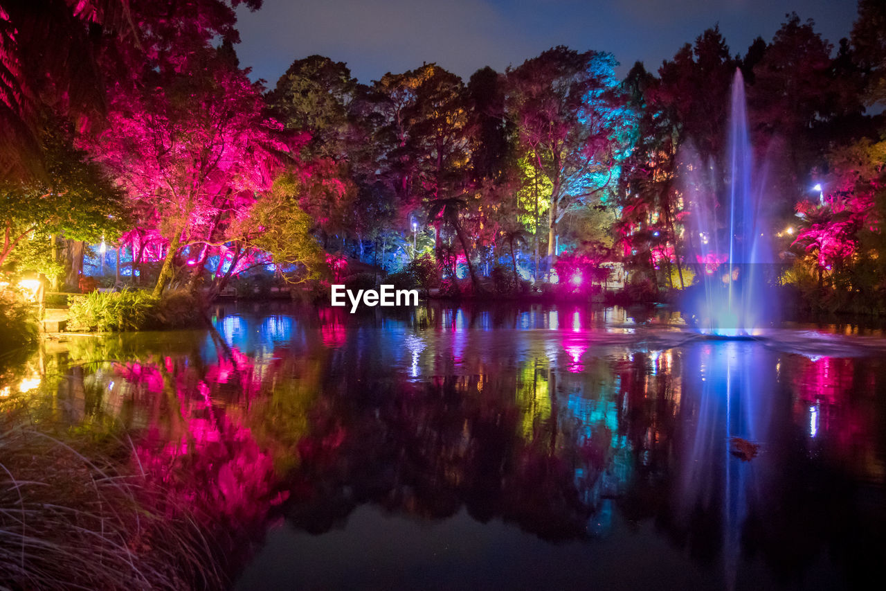 ILLUMINATED TREES BY LAKE AGAINST SKY