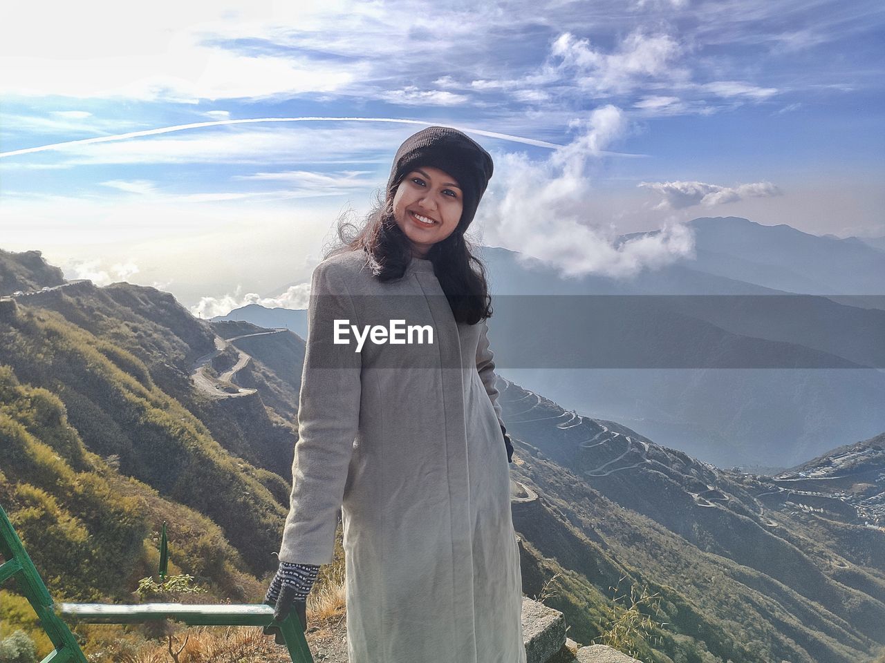 Portrait of smiling woman standing on mountain against sky