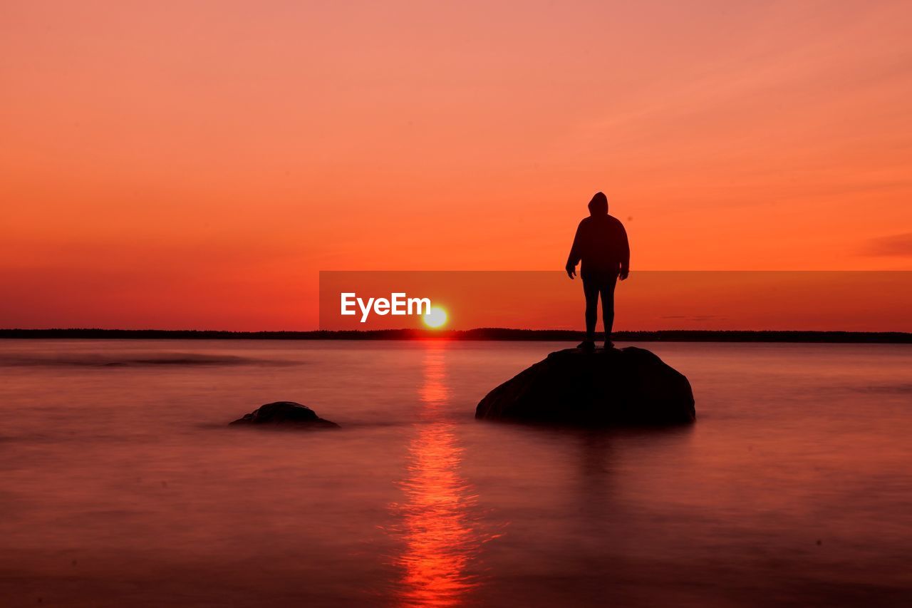 Silhouette man standing on beach against sky during sunset
