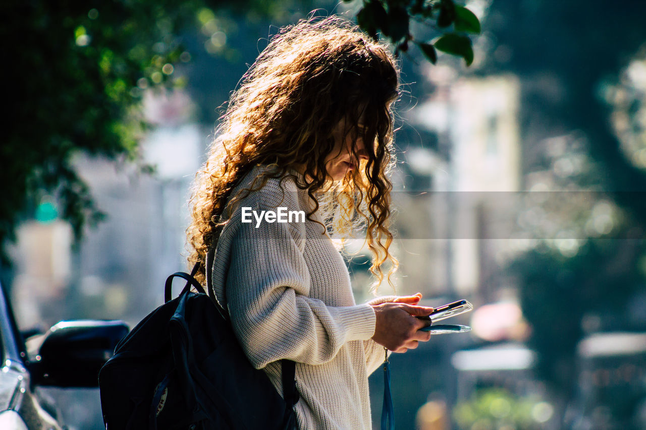 REAR VIEW OF WOMAN USING MOBILE PHONE