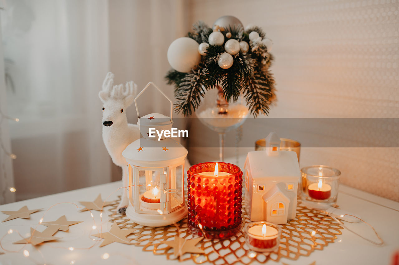 Burning white and red candles, a candlestick of lantern form on napkin, figurinemoose, garlands