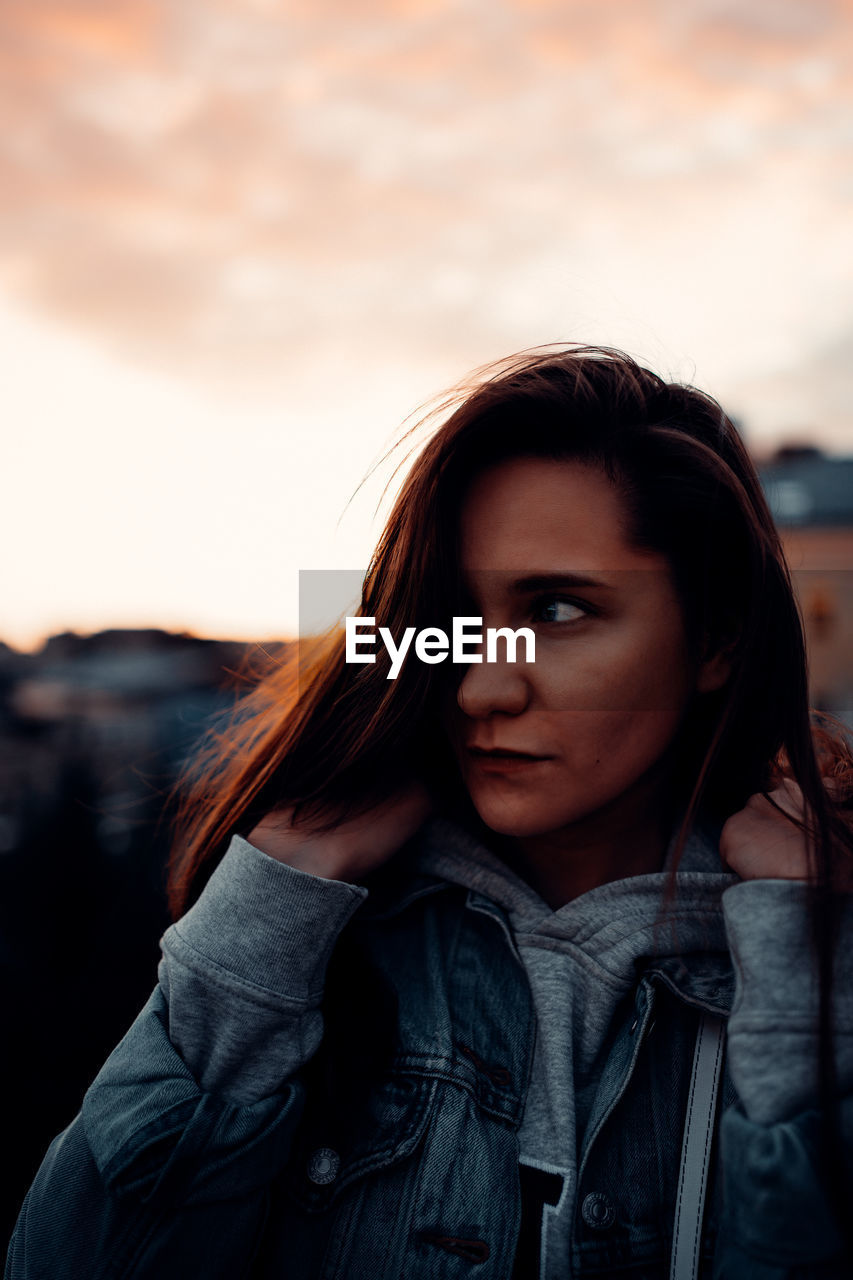 PORTRAIT OF YOUNG WOMAN LOOKING AWAY AGAINST SKY