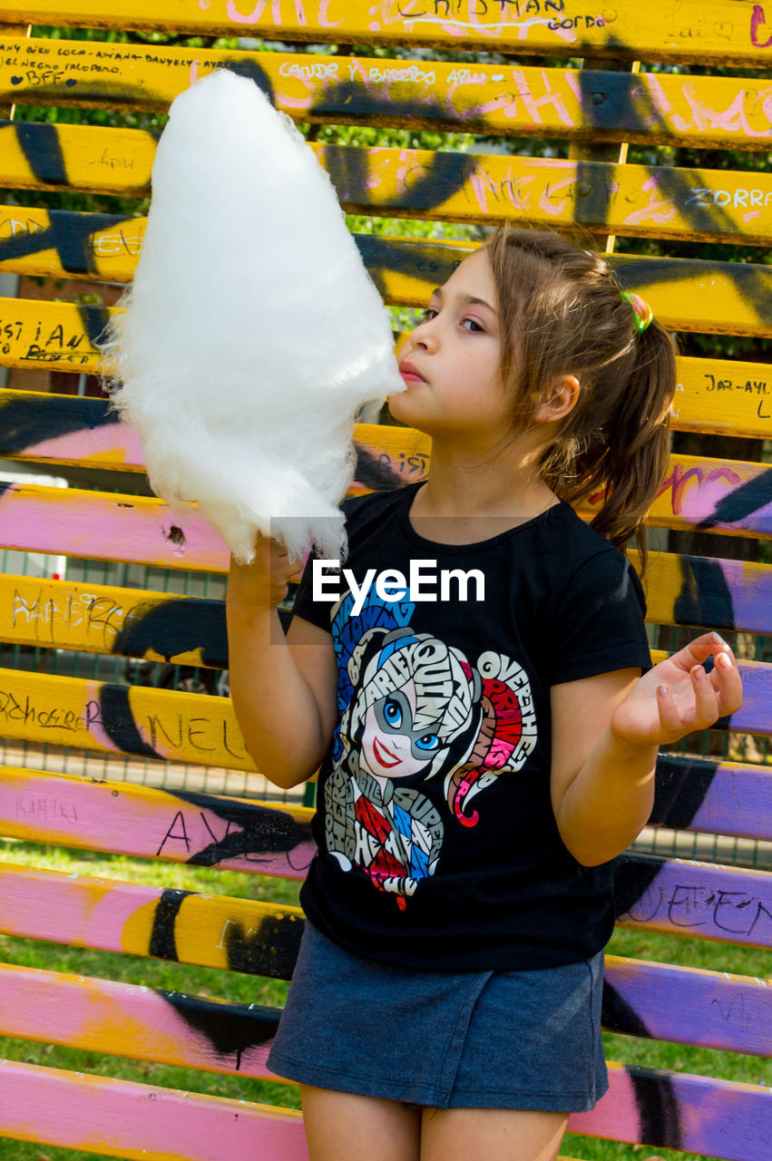 Girl eating cotton candy while standing against wall