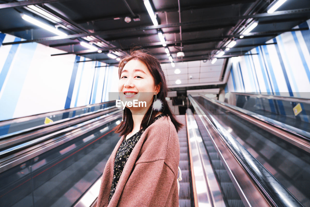 PORTRAIT OF A SMILING YOUNG WOMAN ON ESCALATOR