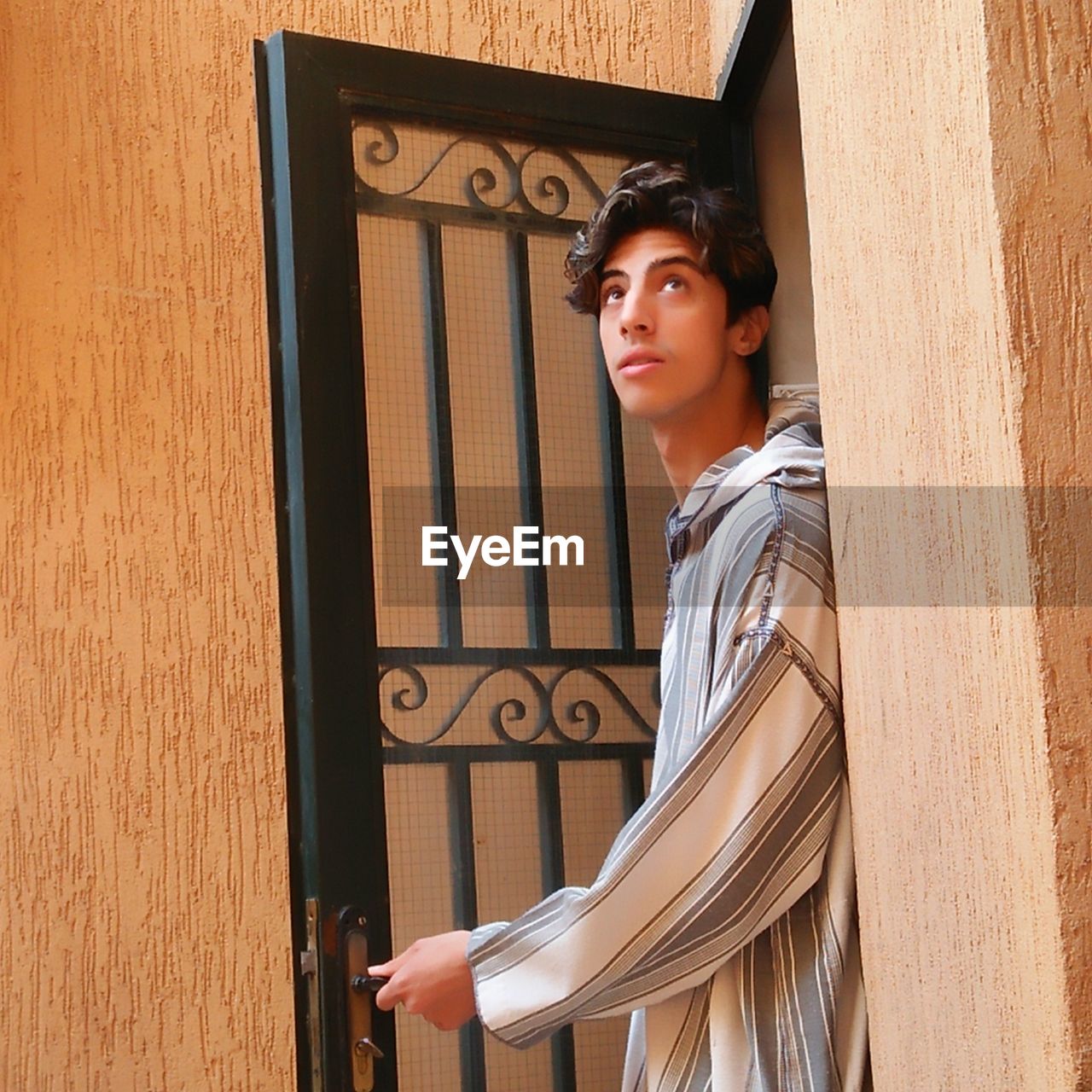 Young man looking away while standing against door
