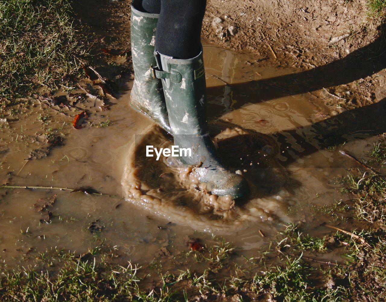 LOW SECTION OF PERSON STANDING ON WET PUDDLE