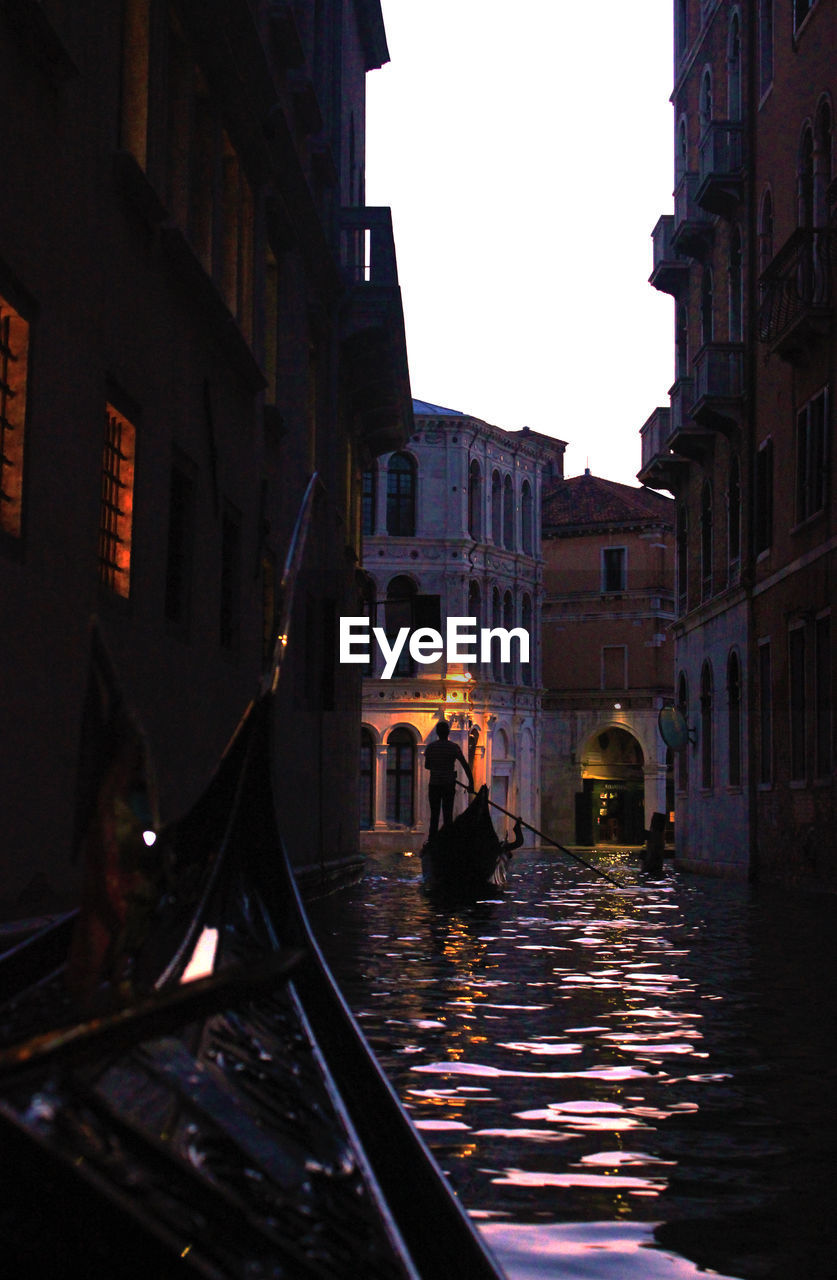 Gondolas on canal amidst buildings in city at sunset