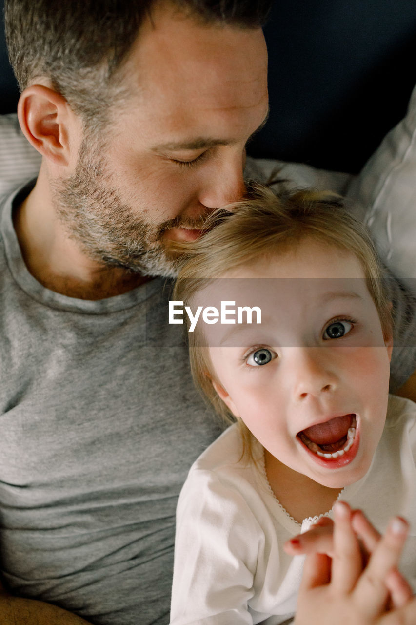 Portrait of girl shouting while lying on bed with father in bedroom