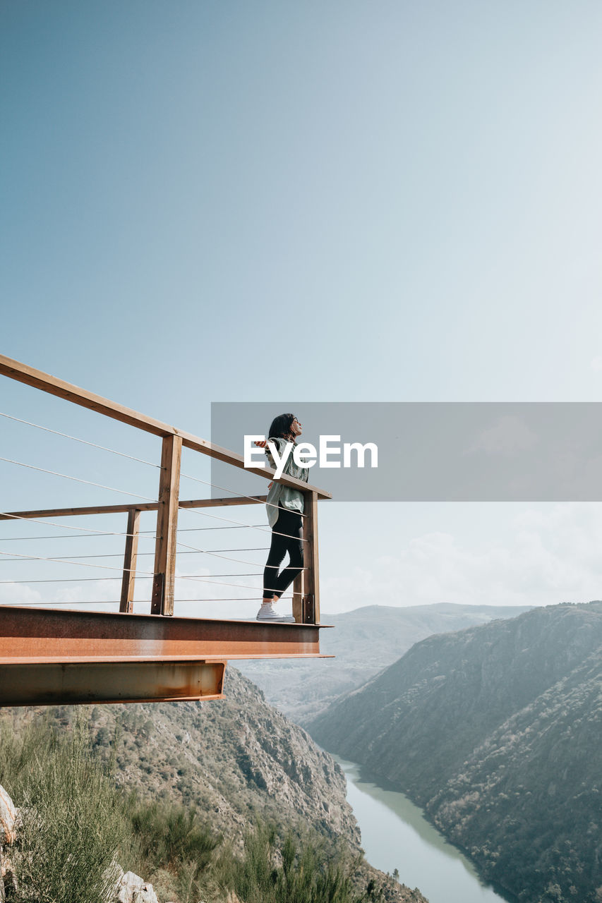 Low angle view of woman standing by railing against sky