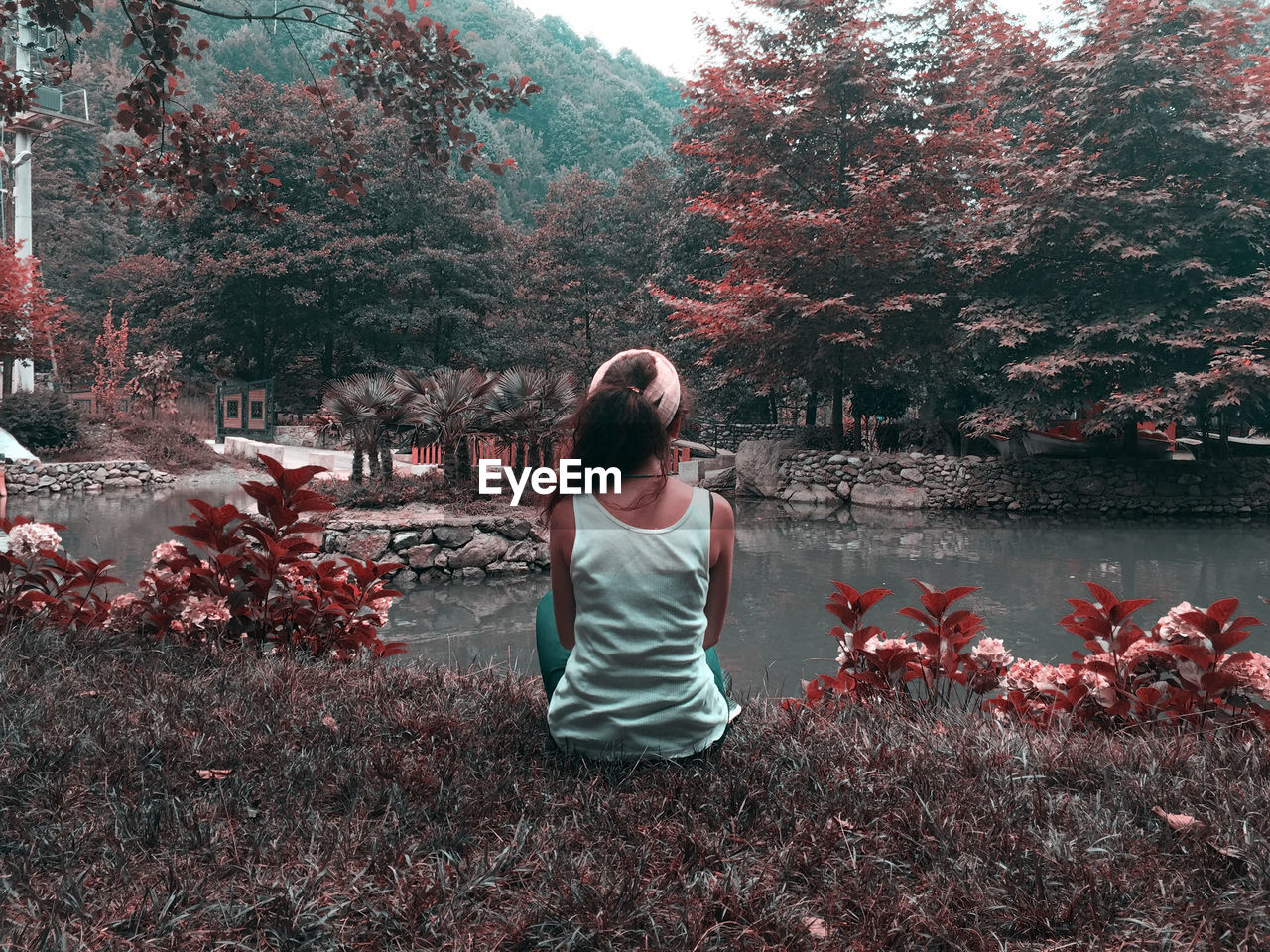 REAR VIEW OF WOMAN SITTING BY PLANTS AGAINST LAKE