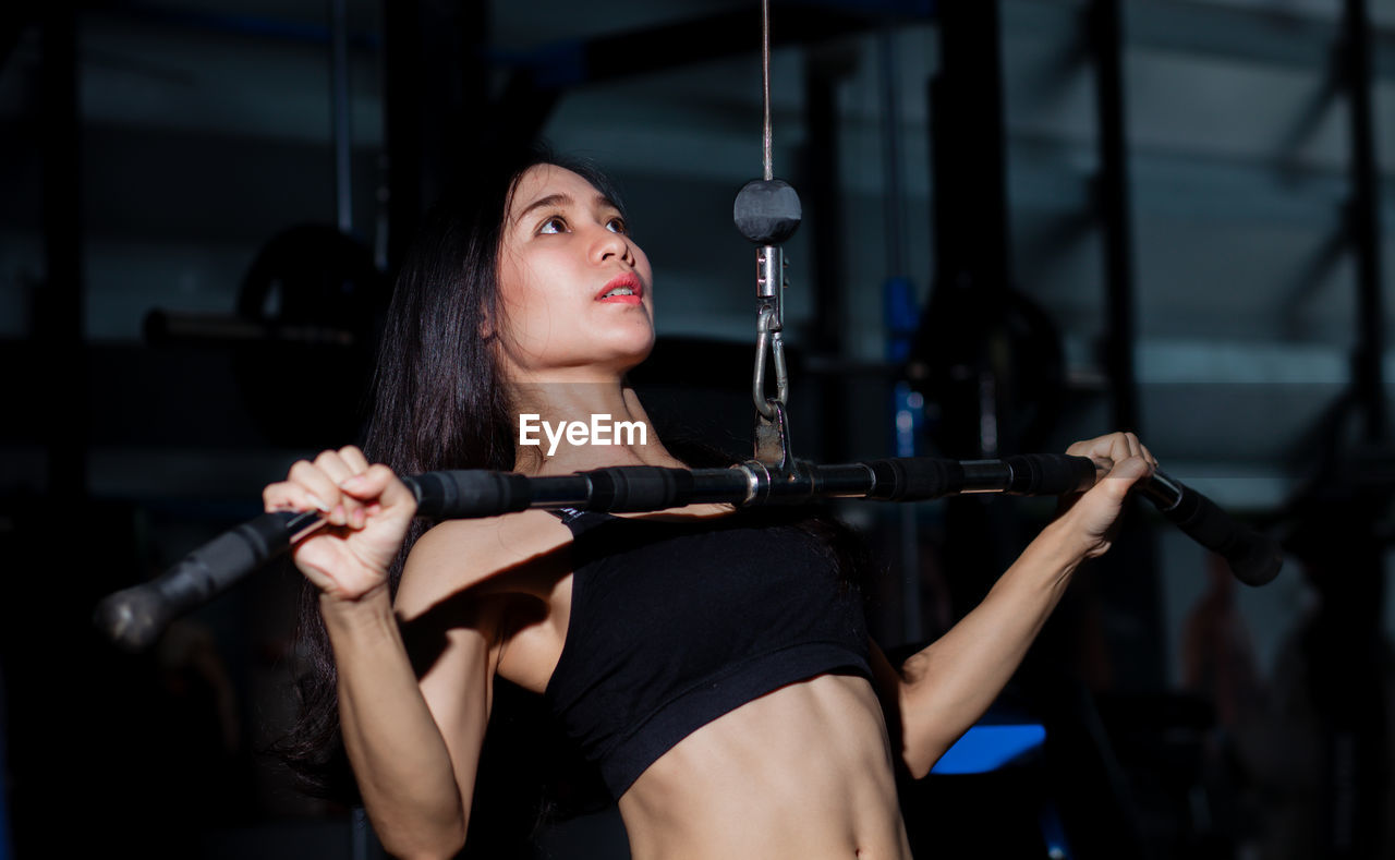Young woman looking away while exercising on equipment in gym