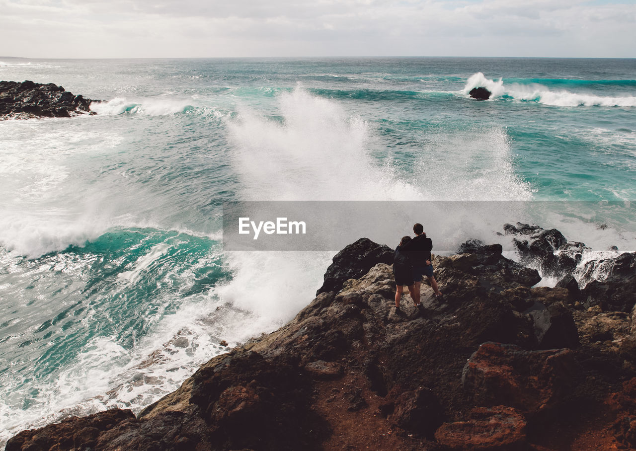 Rear view of couple standing on cliff by sea 