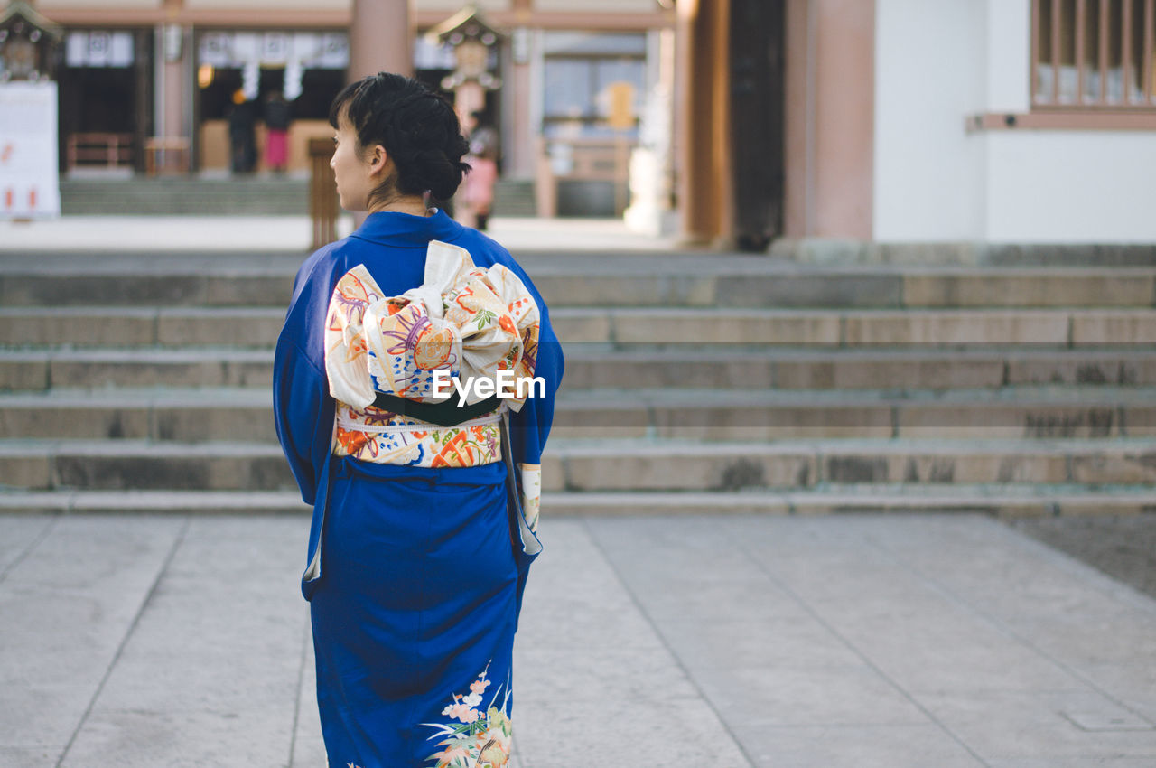 Rear view of woman standing on footpath against building