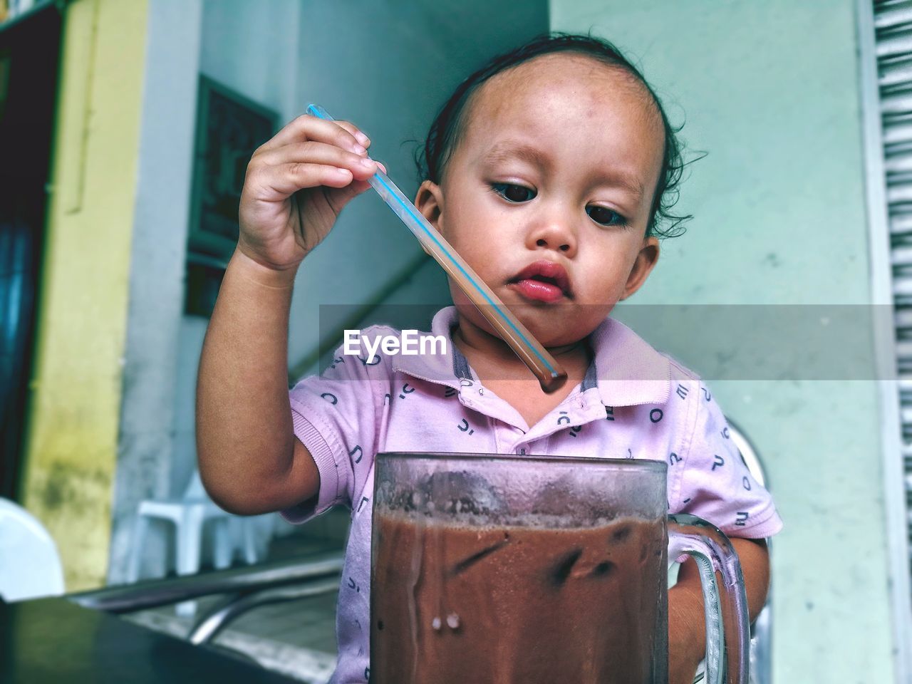 Cute baby boy holding straw in iced coffee at home