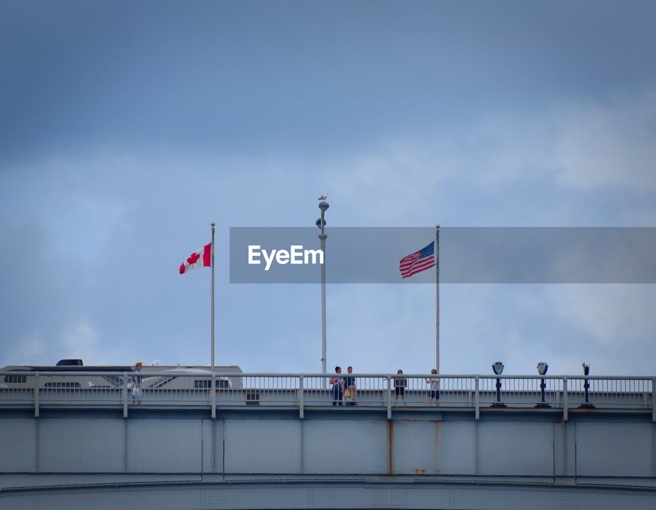 Low angle view of two flags in canadian usa border against sky in city
