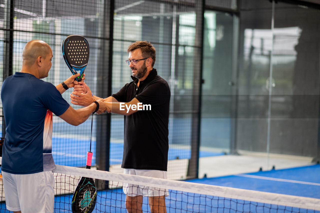 Monitor teaching padel class to man, his student - trainer teaches boy how to play padel on indoor 