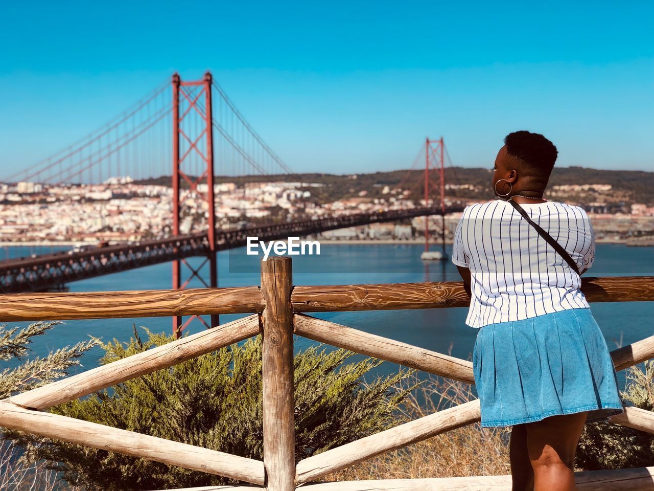 Rear view of woman looking at april 25th bridge over tagus river against sky