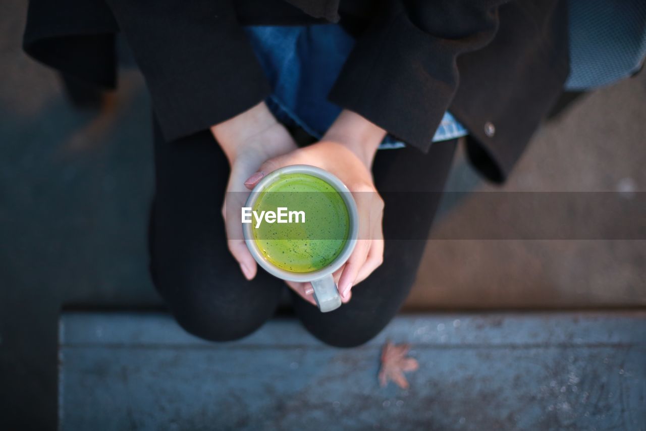 Midsection of woman holding matcha tea while sitting outdoors