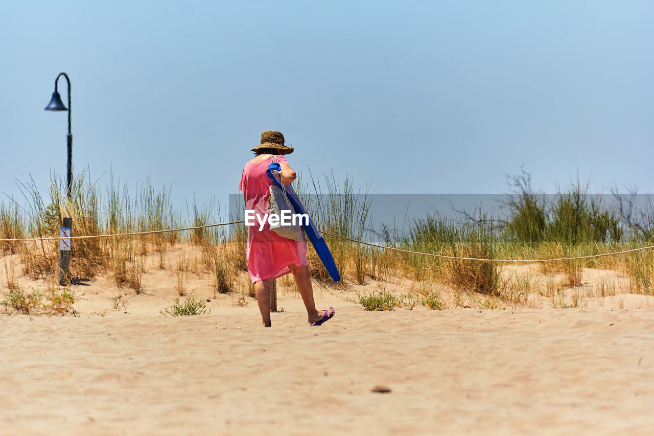 full length, sand, land, nature, sky, one person, natural environment, beach, walking, women, clothing, adult, day, childhood, child, copy space, sea, female, landscape, plant, vacation, clear sky, motion, sand dune, outdoors, leisure activity, holiday, casual clothing, sunny, blue, travel, person, hat, on the move, lifestyles, trip, desert, sunlight, rear view