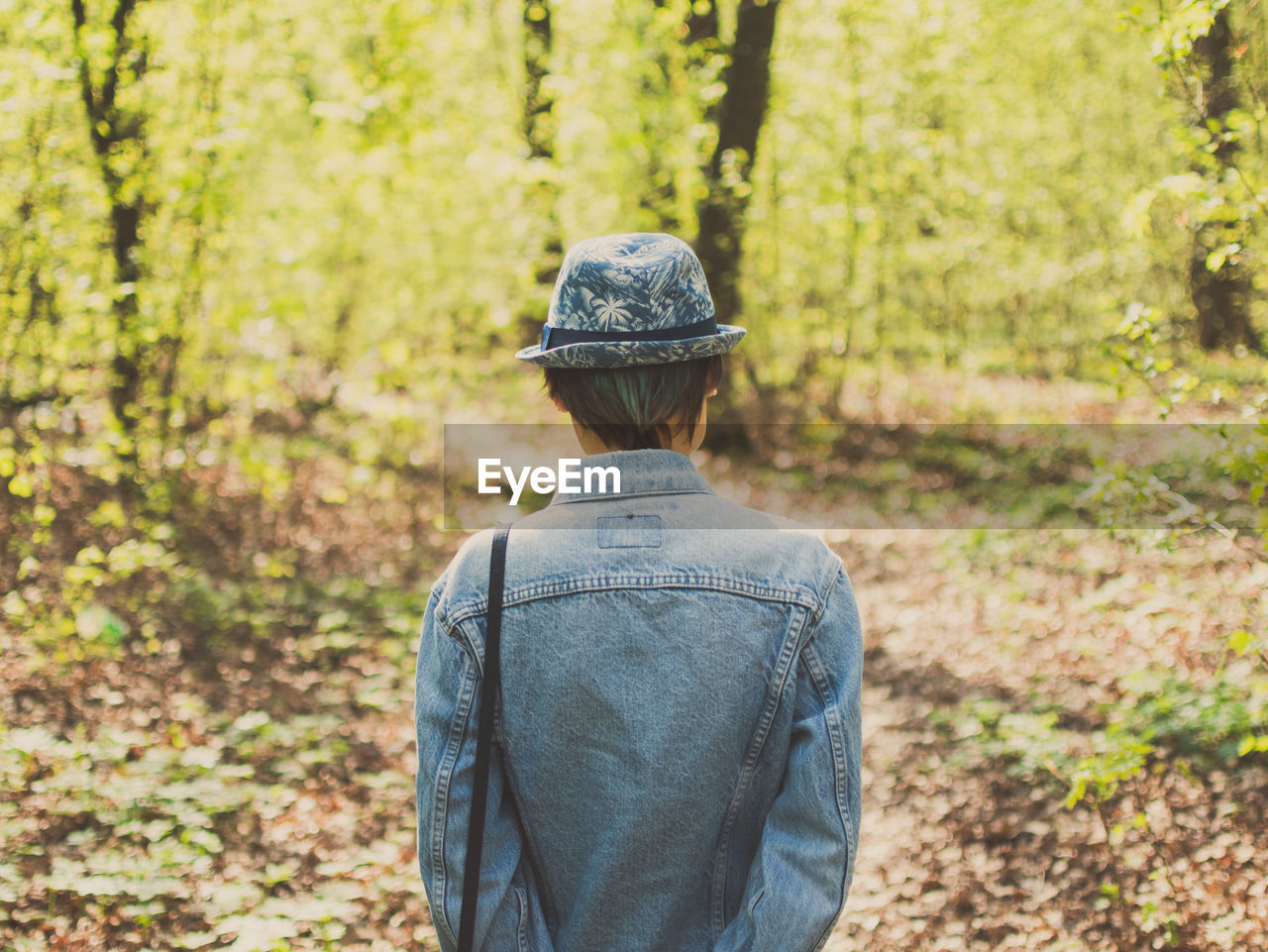 Rear view of woman wearing denim shirt and hat while standing in forest