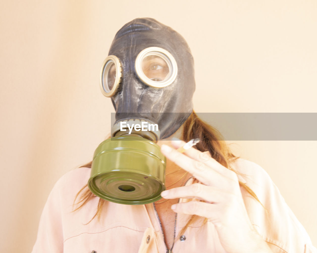 Woman wearing gas mask holding cigarette against wall